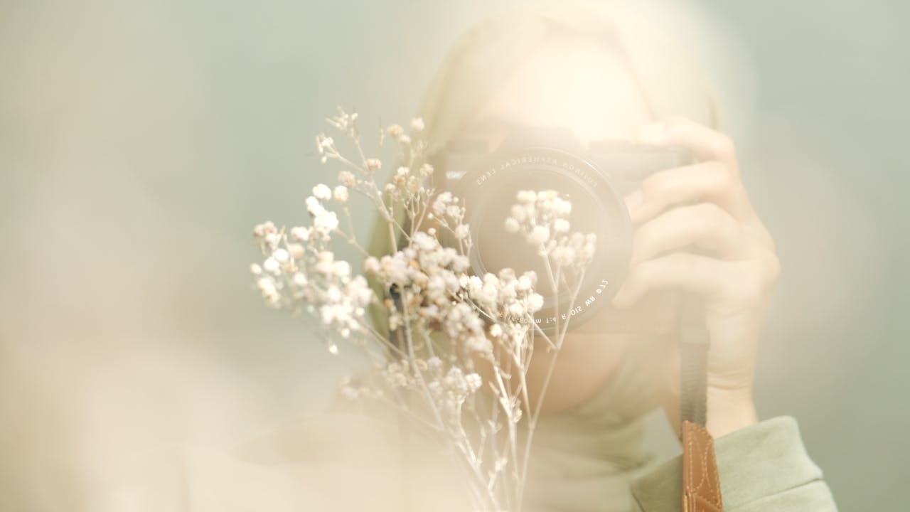 Blurry artistic portrait showing a person with a camera and delicate flowers.